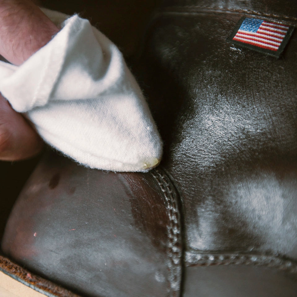 Person applying otter wa boot wax to a boot with a white cloth