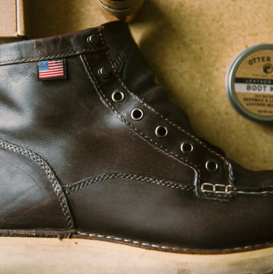 Close-up of a black leather boot with an American flag patch on a wooden surface.