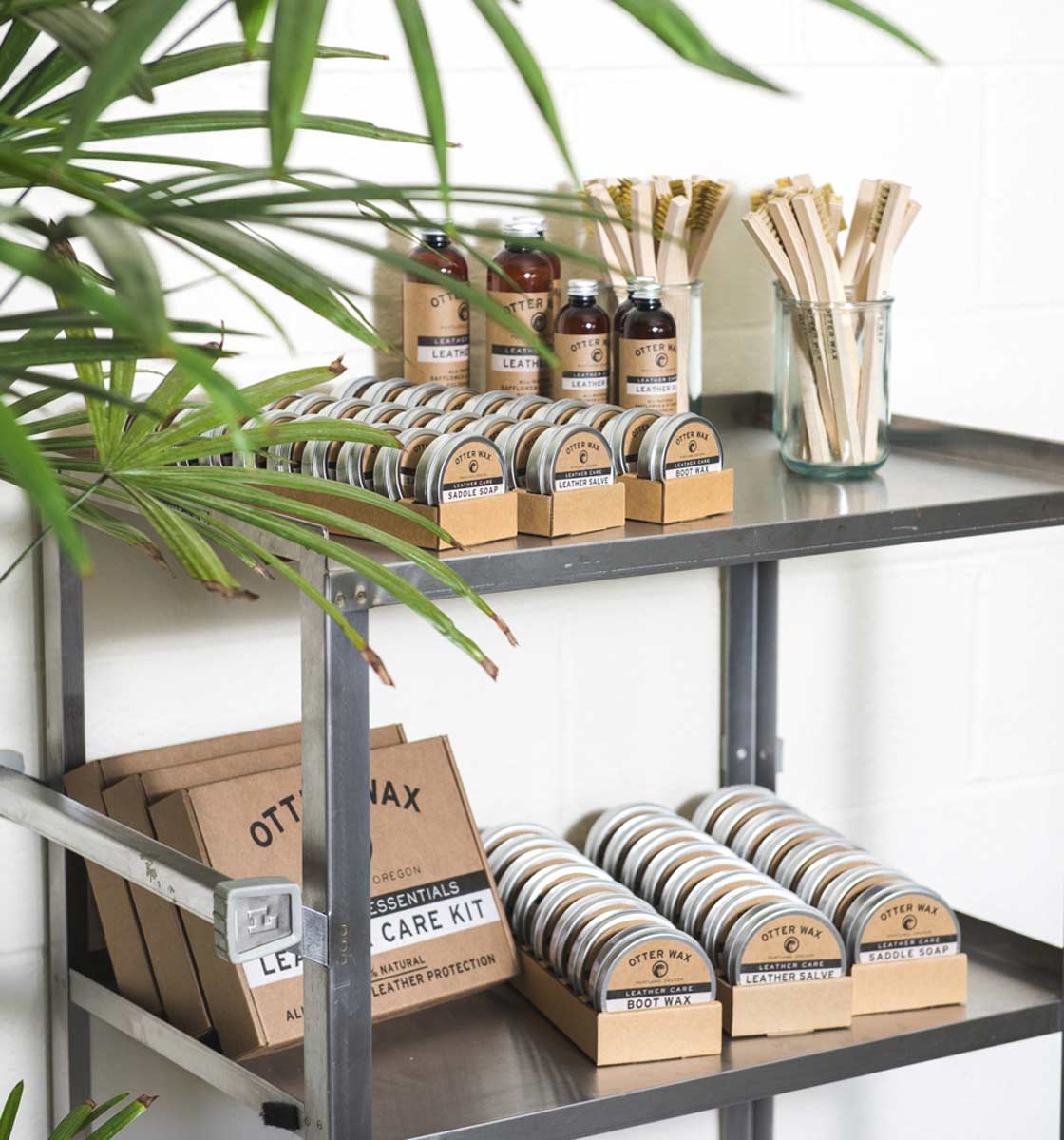 Display shelf with Otter Wax leather care products including Leather Salve, Saddle Soap, Boot Wax, and Leather Oil bottles beside jars of wooden applicators.