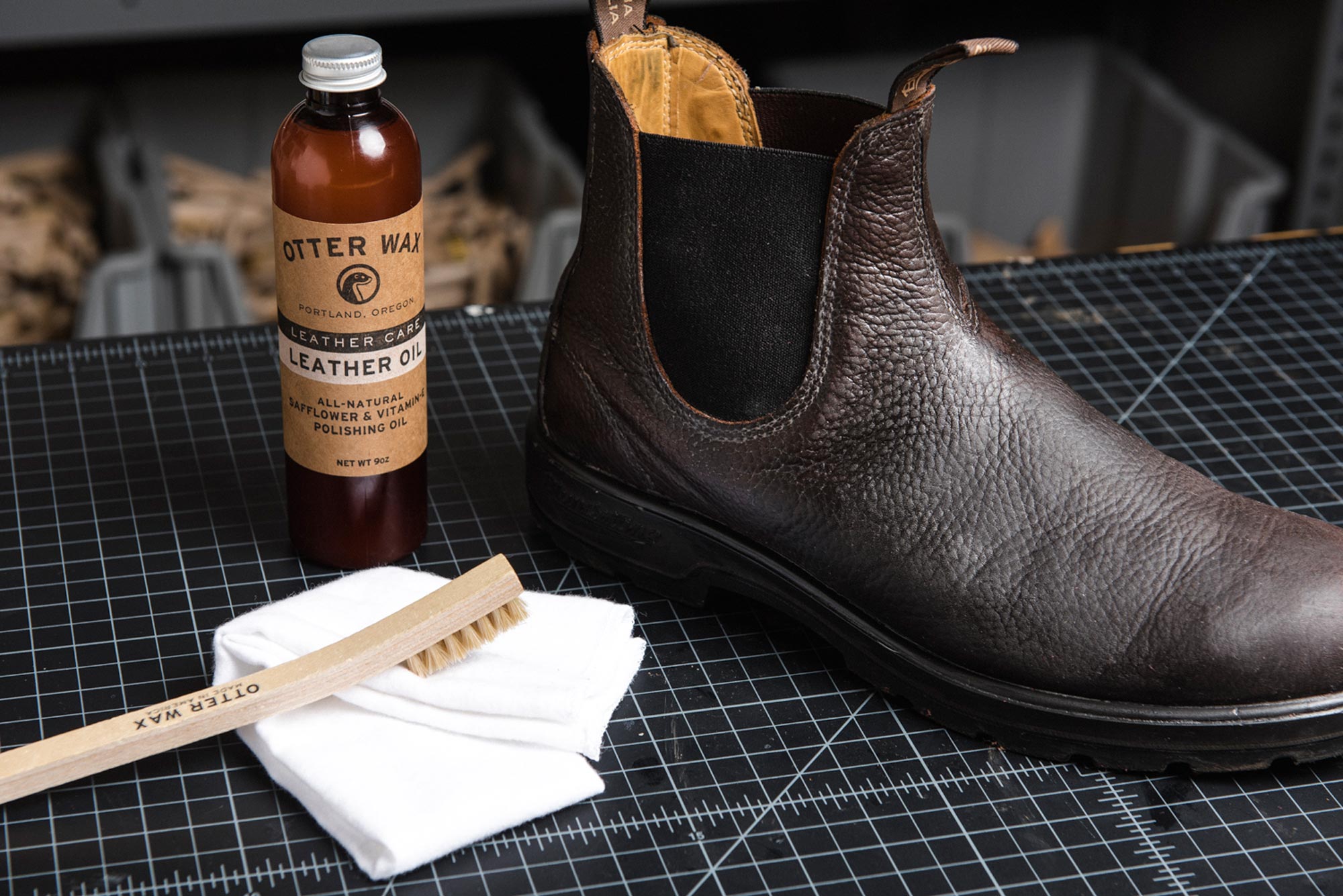bottle of otter wax leather oil next to a leather boot and horsehair brush