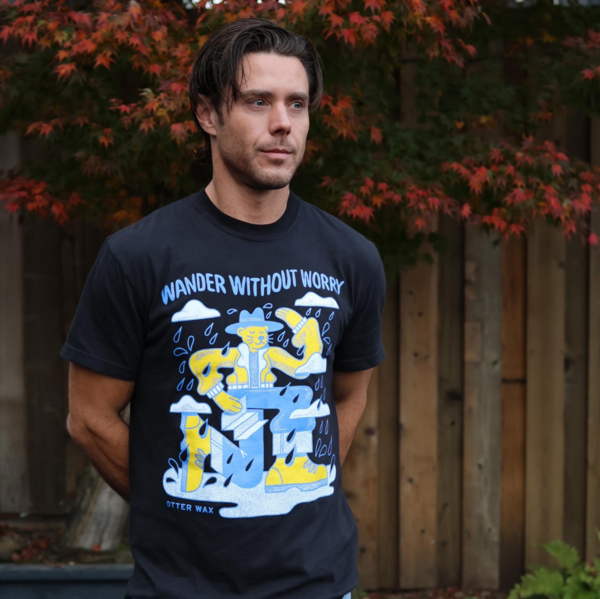 Man wearing a black t-shirt with colorful graphic design and text, standing outdoors.