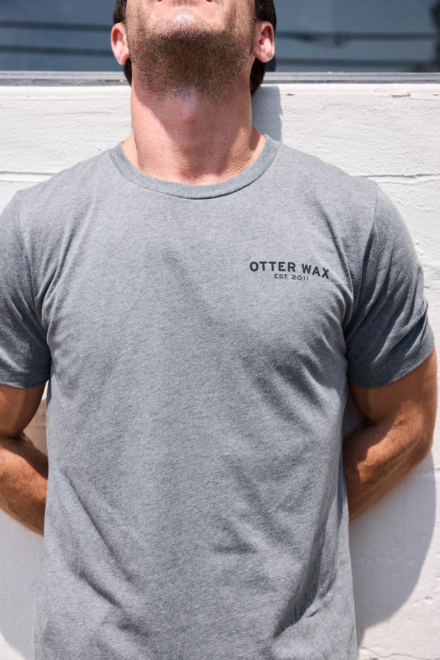 Man wearing a gray t-shirt with 'Otter Wax' logo against a light-colored wall.