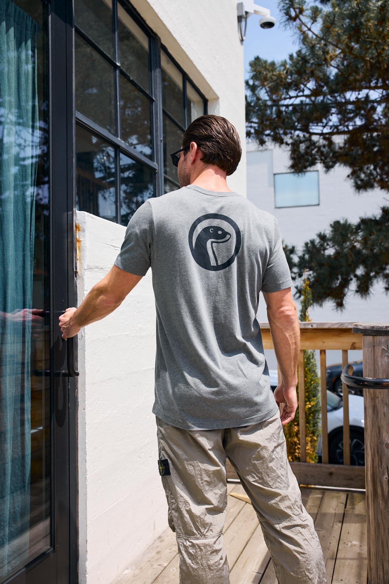 Man wearing a gray t-shirt with a logo on the back, standing outside a building.