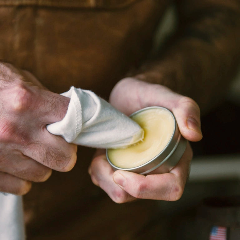 Person applying otter wax boot wax from a tin with a cloth.